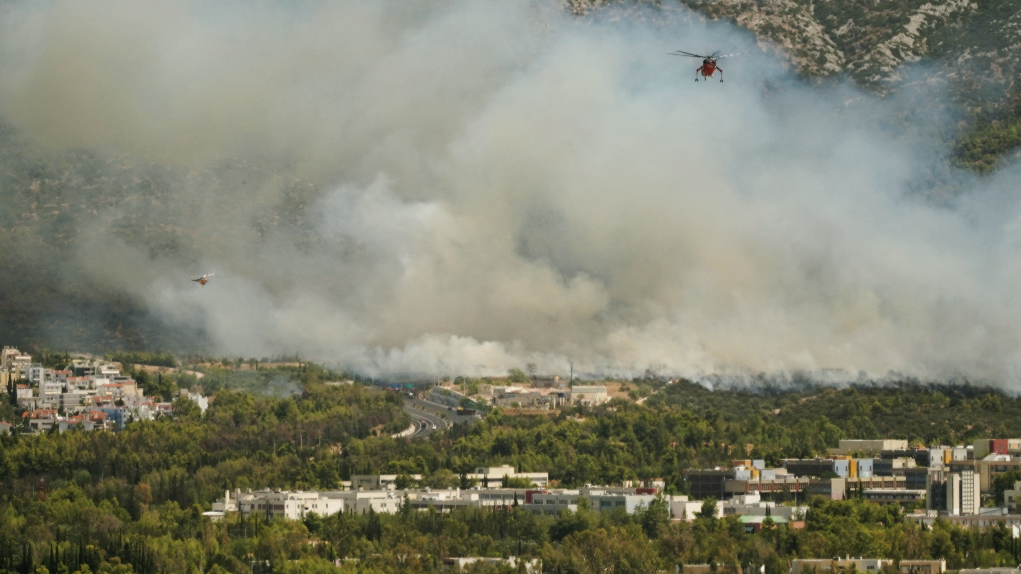 Helicópteros de extinción de incendios sobrevoan un incendio forestal en Atenas (Stamos Prousalis/Reuters)
