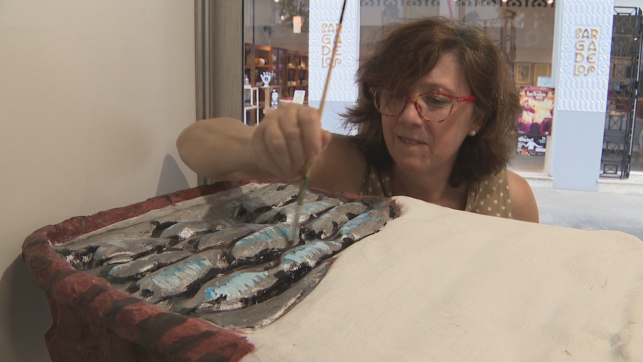 A artesá do cartón pedra pinta as sardiñas na patela dunha peixeira