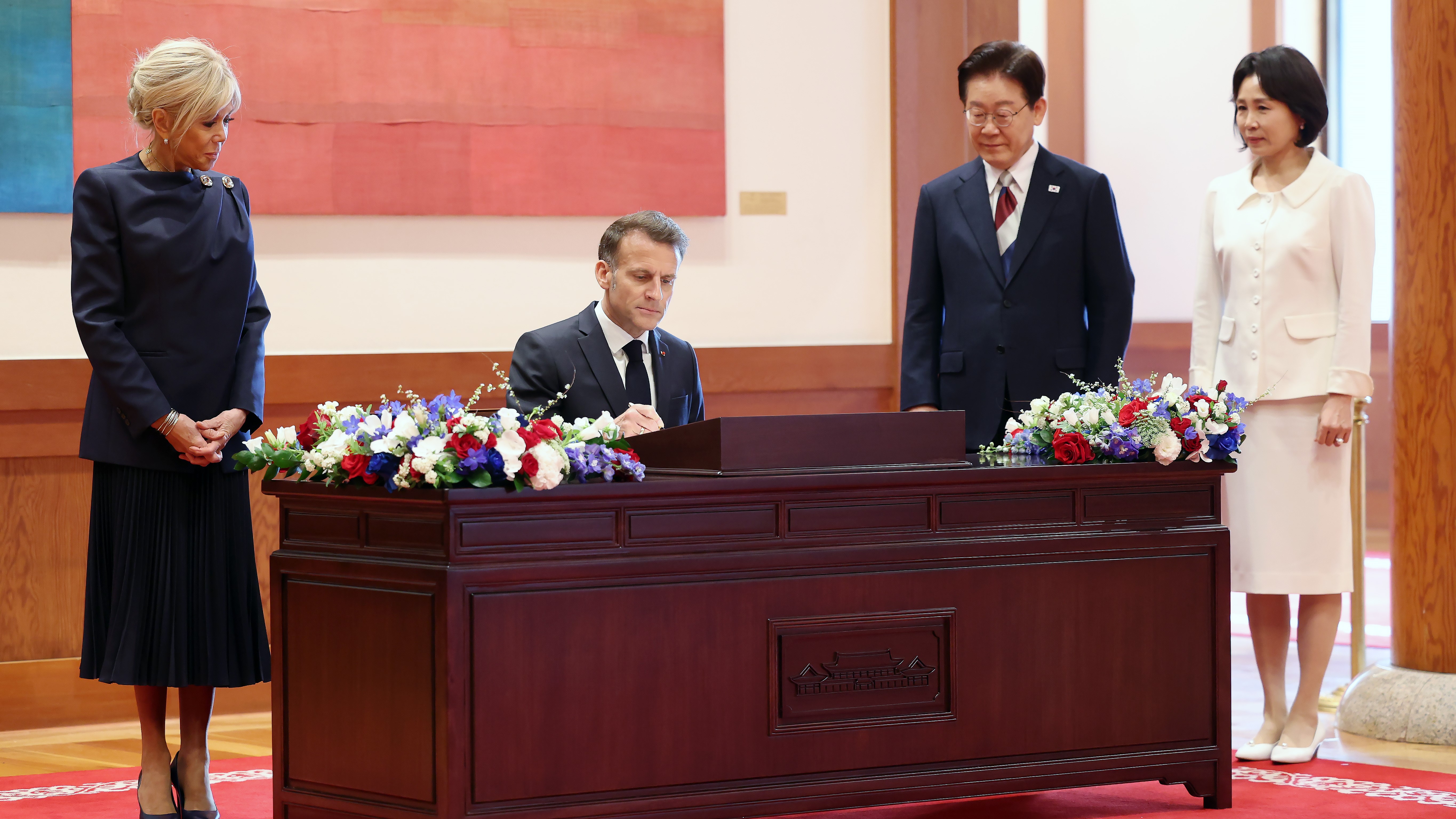 O presidente francés, Emmanuel Macron, acompañado pola súa dona, Brigitte Macron, asina no libro de convidados en presenza do presidente de Corea doSur, Lee Jae Myung, e a súa esposa, Kim Hea Kyung, este venres no pazo presidencial de Seul (Europa Press)