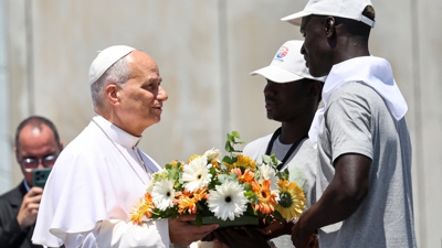 León XIV recolle da man de dous migrantes unha coroa de flores que lanzou á auga no porto de Arguineguín, en recordo dos que faleceron no mar (Reuters/Yara Nardi)