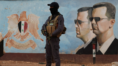 Un membro do antigo grupo Hayat Tahrir al-Sham á beira dunha imaxe de Bashar al-Assad.  REUTERS/Yamam Al Shaar
