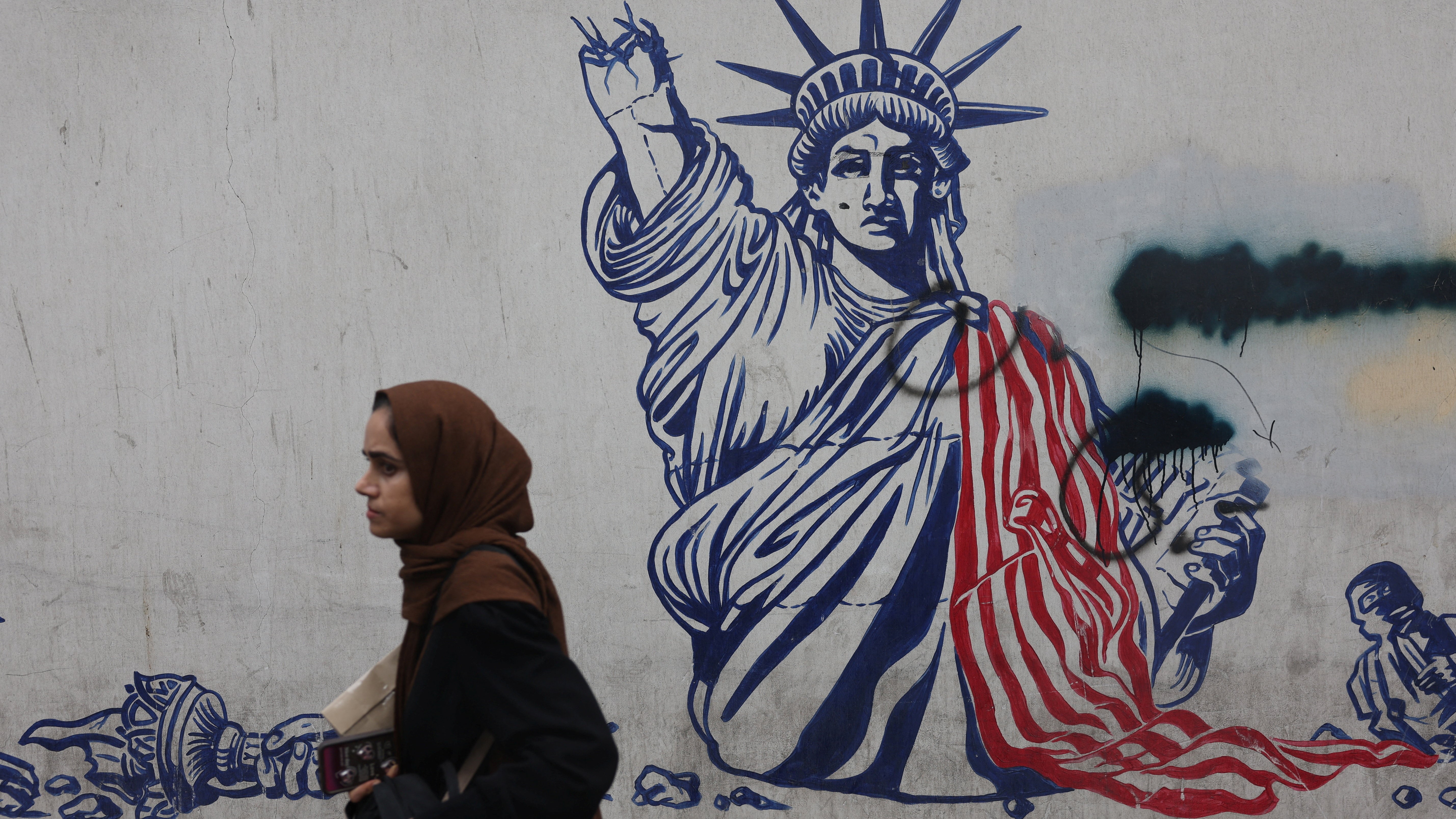 Unha muller camiña diante dun mural antiestadounidense en Teherán (WANA/Majid Asagaripour/vía Reuters)