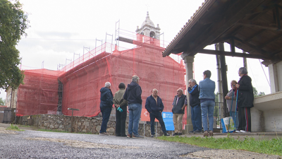 Veciños de Vilasantar ao pé do Santuario da Nosa Señora da Laxe, cuberto cunha lona polas obras de restauración